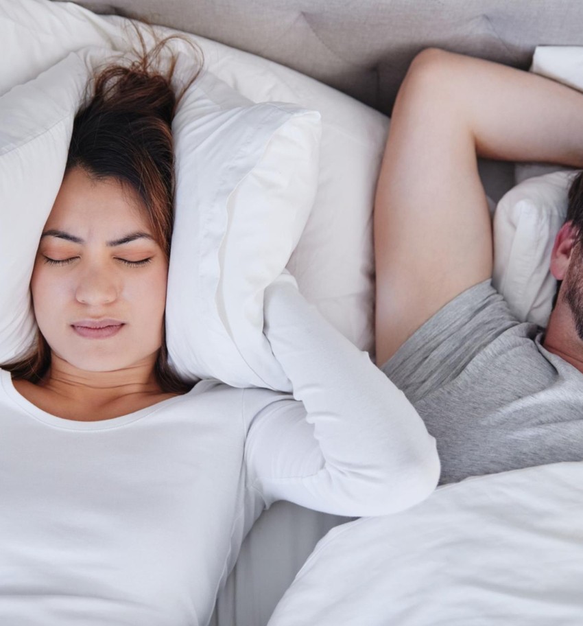 woman covering her ear with pillow while sleeping